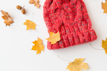 Fototapeta na wymiar season, headwear and clothes concept - knitted woollen hat and fallen autumn leaves on white background