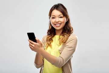 Naklejka premium technology and people concept - happy asian woman using smartphone over grey background