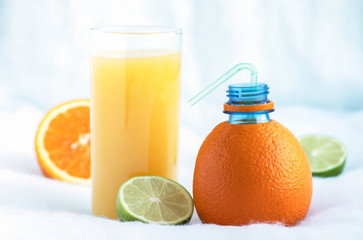A bottle made of natural orange and a glass of freshly squeezed orange juice surrounded by slices of tropical orange and lime fruit.