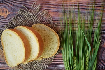 Fresh bread in a wicker basket and green ears on a wooden background.