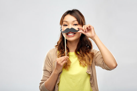 party props, photo booth and people concept - happy asian young woman with big black mustache over grey background