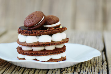 Baking homemade chocolate cake with biscuit, meringue and macaroons in white plate on wooden table. Festive sweet dessert birthday decoration macarons