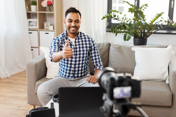 blogging, videoblog and people concept - indian male blogger with camera recording video blog and showing thumbs up at home
