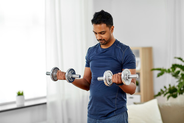 fitness, sport, weightlifting and bodybuilding concept - indian man exercising with dumbbells at home