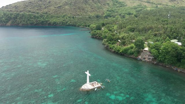Aerial drone view of a cross and sunken cemetery with large volcanos behind (Camiguin, Philippines)