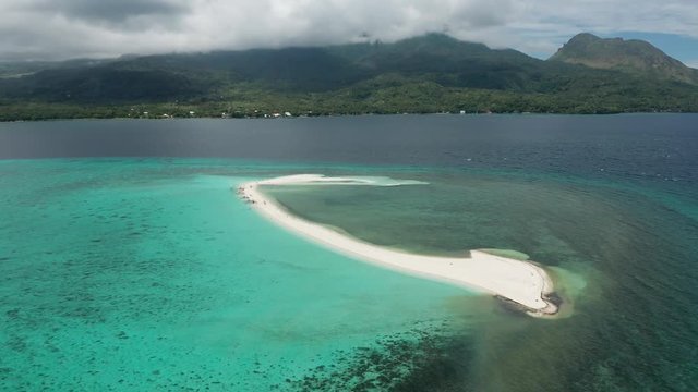 Aerial drone view of a tiny sandy island surrounded by shallow reef off the coast of a lush green island (White Island, Camiguin)