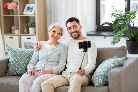 family, generation and people concept - happy smiling senior mother with adult son taking picture by selfie stick at home