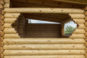 Gazebo made of logs. Window in wooden terrace. Elements of wooden construction.