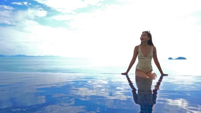 Asian model posing for the picture in infinity pool wearing monokini swimming suit and sun glasses on sea background
