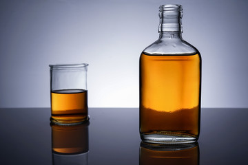 A backlit of a glass bottle and jar with golden liquid 