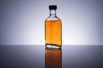 A backlit of a glass bottle and jar with golden liquid 