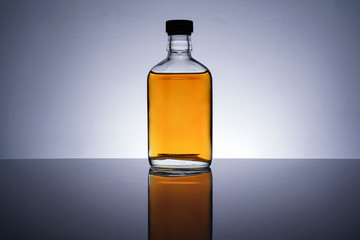 A backlit of a glass bottle and jar with golden liquid 