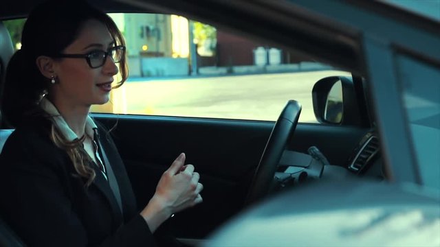 Attractive caucasian business woman in a parked car while talking on the phone. She begins serious, then becomes happy. Slow motion.