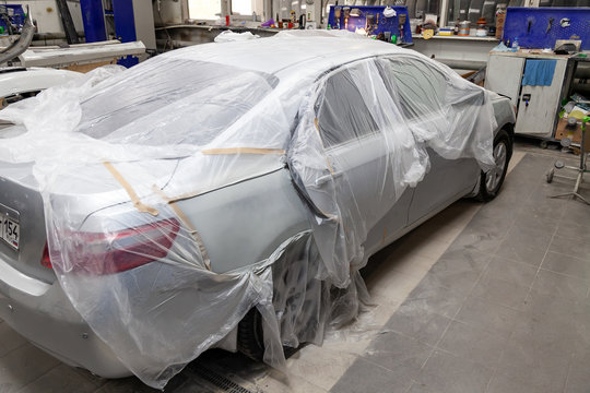 A broken car covered with a protective film from splashing paint in a spray booth in a car body repair shop before it is painted and repaired. Auto service industry.