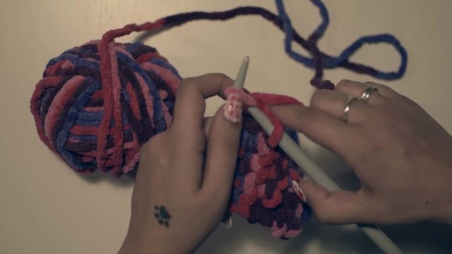 Topview on woman knitting with stitches, crafting a pink and purple fabric.