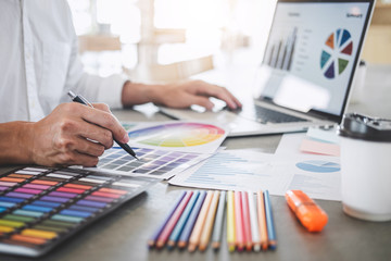 Young creative graphic designer working on project architectural drawing and color swatches, selection coloring on graphic chart with work tools and equipment