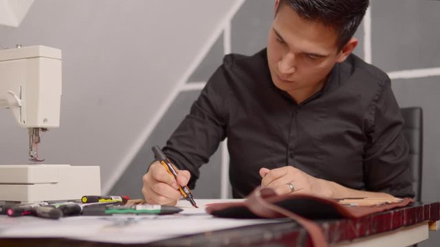 Young fashion designer chooses a pen and starts painting his sketch with a thick colored pencil.