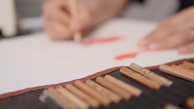 Person is sketching something with crayons. In the foreground are different pens.