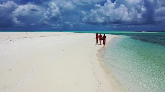 drone extreme long shot of three young ladies practicing cat walk on white sand beach, with crystal clear sea