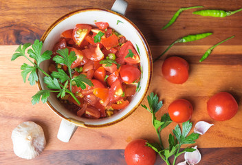 Top view of tomato salad with basil, olive oil, garlic, chilli and balsamic vinegar in bowl over wooden background