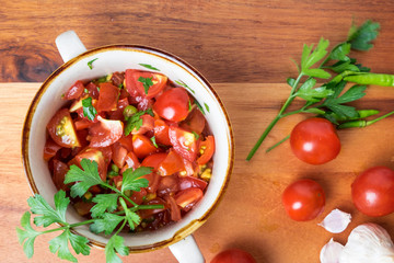 Top view of tomato salad with basil, olive oil, garlic, chilli and balsamic vinegar in bowl over wooden background