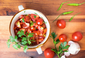 Top view of tomato salad with basil, olive oil, garlic, chilli and balsamic vinegar in bowl over wooden background