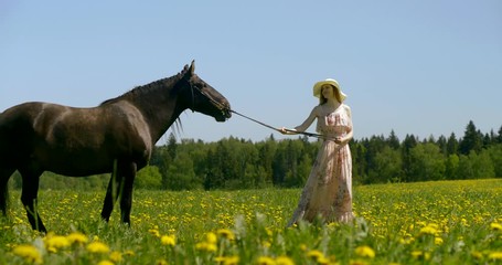 lady in long summer dress and hat holds brown horse halter - Powered by Adobe