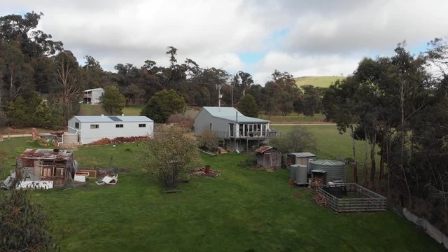 Drone footage of a small country homestead in the Australian (Victorian) countryside. Steel house, outbuildings and water tanks. Gum trees and green grass