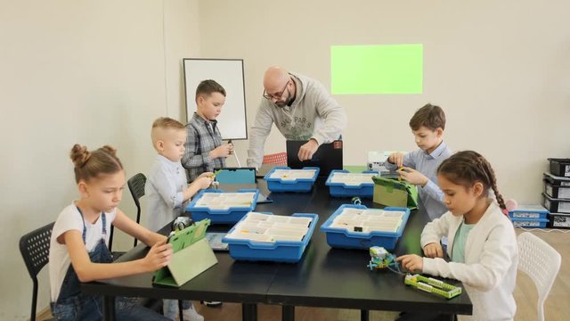 Group of young kids try to design their first plastic robots and cars at the engeniiring lesson slow motion