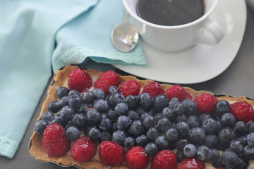Cake with raspberries and a cup of coffee on a gray table. Homemade tart with berry. Top view.