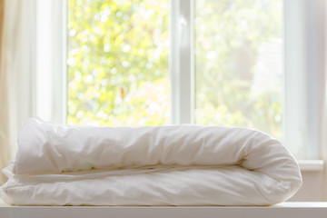 A white duvet is lying on the dresser against the blurred background of the window.