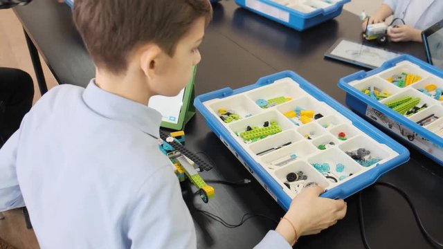 Caucasian teenage boy builds his plastic helicopter using the details from the box at the engineering lesson slow motion