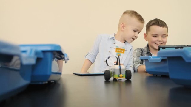 Cute blond child tryies his skills in moving the bright robopt cat on the table during class slow motion