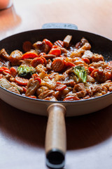 Hot cast iron pan with fresh stir fry with different vegetables and pieces of meat 