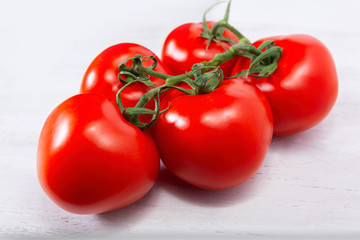 Group of five fresh, ripe red tomatoes, still connected through the green stem on the white background
