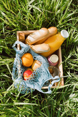 Various fruits and cold beverages in a wooden box on a grass, summer zero waste picnic concept