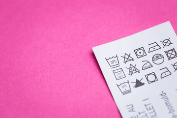 Label with information for washing and caring for clothes close-up. On a pink isolated background.