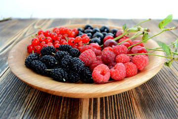 Different delicious fresh summer berries cherry, currant, blackberry in wooden plate on wooden background 