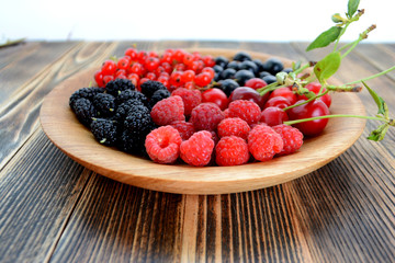 Different delicious fresh summer berries cherry, currant, blackberry in wooden plate on wooden background 