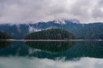 Obraz na płótnie Canvas Montenegro, Black lake nature in durmitor national park landscape next to zabljak, green forested island mirroring on glassy calm lake water in mystic foggy atmosphere