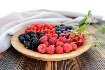 Different delicious fresh summer berries cherry, currant, blackberry in wooden plate on wooden background 