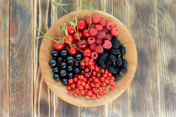 Different delicious fresh summer berries cherry, currant, blackberry in wooden plate on wooden background 