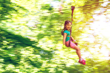 Happy little girl on zip line between trees, panning effect.