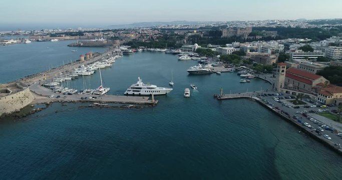 Aerial footage of the old port of Rhodes, including the luxury yachts docked at the old town port and a general view of the old city and bay.