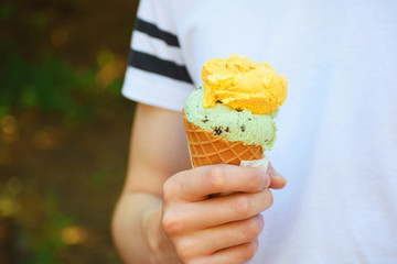 Fresh tasty green yellow ice cream in waffle cone in hand outdoors with copy sppace on white t-shirt.