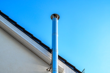 Stainless steel chimney and parts of a roof in front of a bright blue sky.