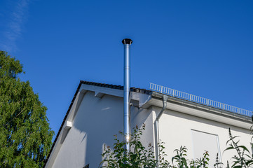 Stainless steel chimney and parts of a roof in front of a bright blue sky.