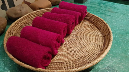 Dark red towel in a wicker plate. Hand towel folded into a roll.