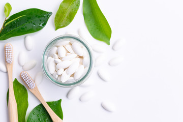 toothpaste tablets in a glass jar with bamboo toothbrushes on white background, eco friendly zero waste living concept.