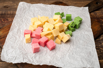 Cheese cubes pink and yellow on crumpled paper background. Wooden cutting board